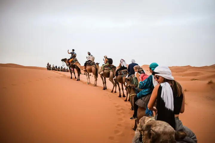 Travellers in a camel caravan entering the dunes