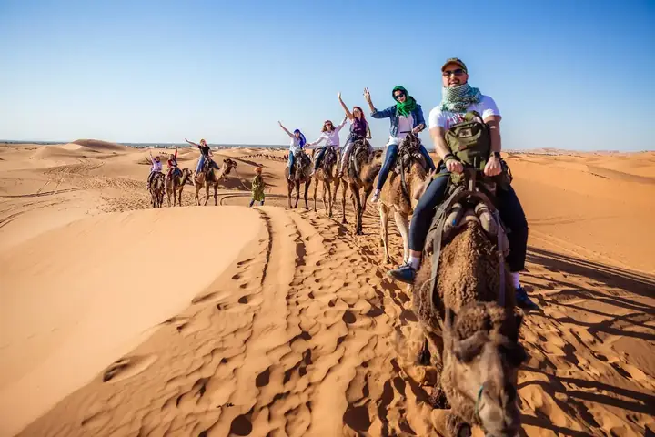 Travellers waving from their camels in Merzouga