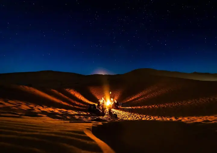 Campfire burning among the dunes under the night sky